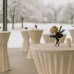 Elegantes Winter-Event in Hotel oder Restaurant mit cremefarbenen Stehtischhussen, Kerzenlicht und goldenen Akzenten – Eventtextilien für Winter-Branding.