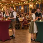 Vom Cannstatter Volksfest 2026 inspirierte Indoor-Feier mit Gästen, bordeauxfarbenen und grünen Stehtischhussen sowie warmen Lichterketten.